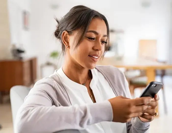 Woman smiling while looking at smartphone in bright indoor setting